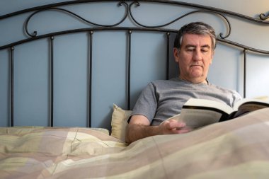 Uykusuzluk çeken bir adam yatakta oturup kitap okuyor..