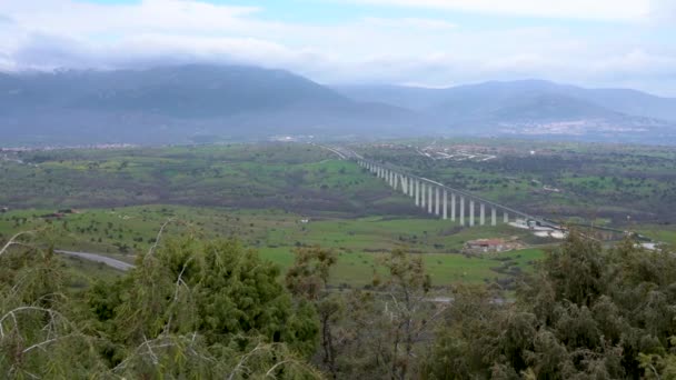 Flygfoto av ett tåg som korsar en vacker bro i ett Spanien genom ett grönt landskap. — Stockvideo
