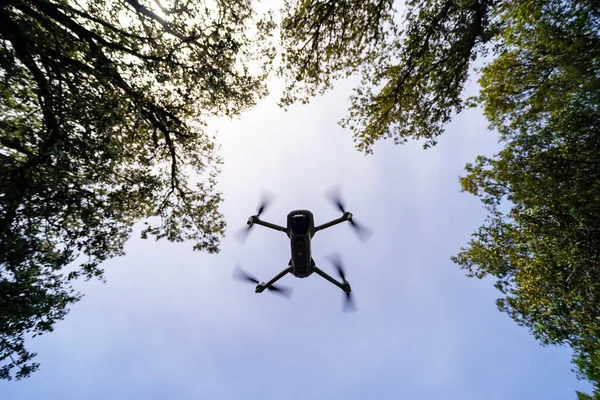 Drone voando no céu azul entre os ramos das árvores. — Fotografia de Stock