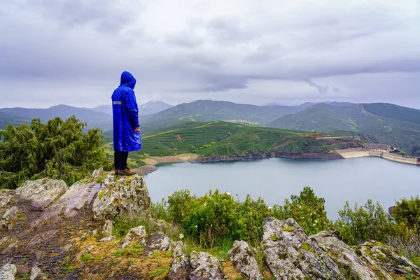 Muž vylezl na skálu na vrchol hory a zamyslel se nad údolím s jezerem. — Stock fotografie