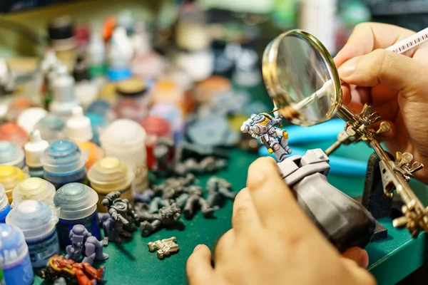 Büyük büyüteçle masa oyununun minyatürlerini boyayan adam.