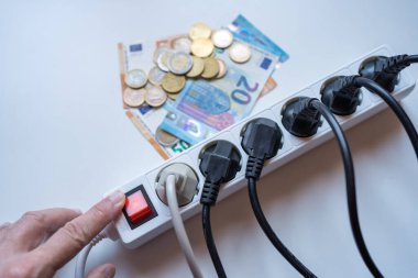 Elektriğin yüksek maliyetini temsil eden fiş şeridini parayla yakan bir adamın eli