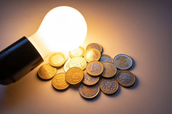 Light bulb lit illuminating coins for the high cost of electricity and inflation