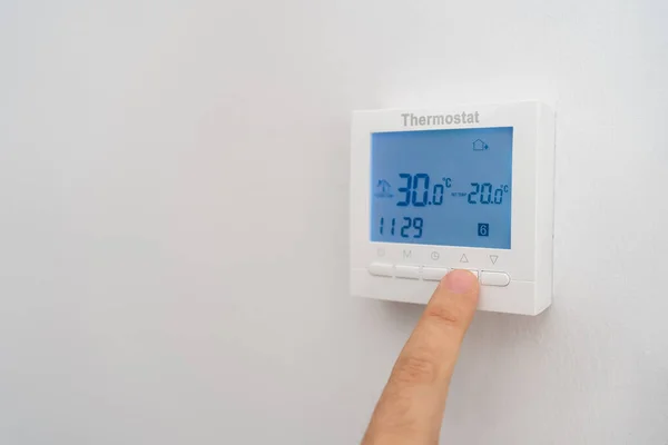 Hand of man raising the thermostat of the air conditioning to save cost by the high inflation
