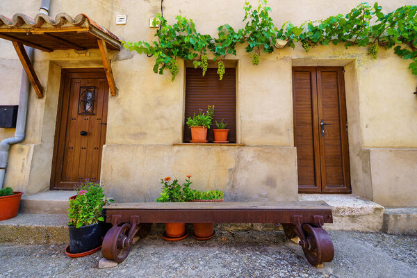Nice facade of stone houses with a vine with grapes climbing the wall and wooden bench at the door