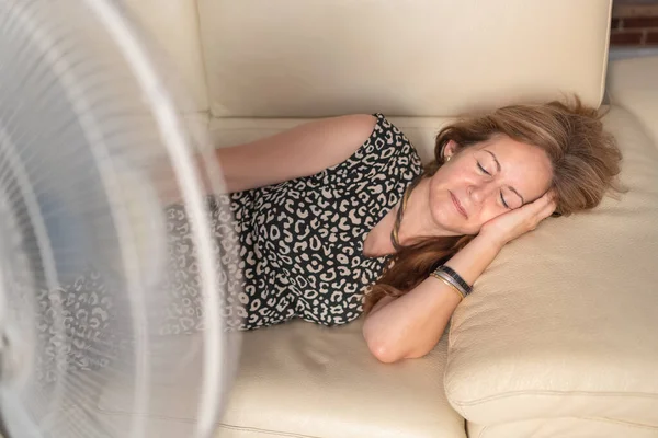 Kanepede uzanmış, önünde yelpazesi olan bir kadın yazın temiz hava aldırıyor.