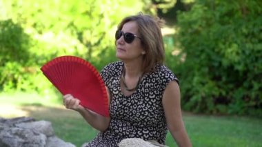 Mature woman slowly fanning herself for fresh air in the summer heat wave, slowmotion