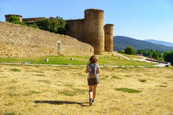 Woman strolling through the countryside in summer with a medieval castle in the background on the hill, Barco de Avila, Spain