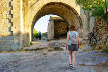 Tourist woman crossing an old stone bridge at the entrance of a village in Castile, Puente Congosto