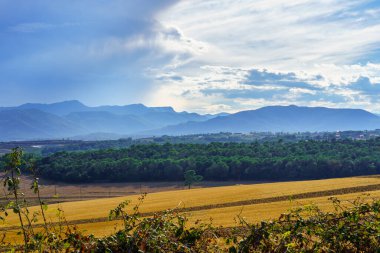Storm clouds over the high mountains with tillage field in the foreground at sunset.