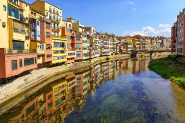 Houses of colorful colors on the banks of the river and reflection in the calm water on a sunny day, Girona, Catalonia