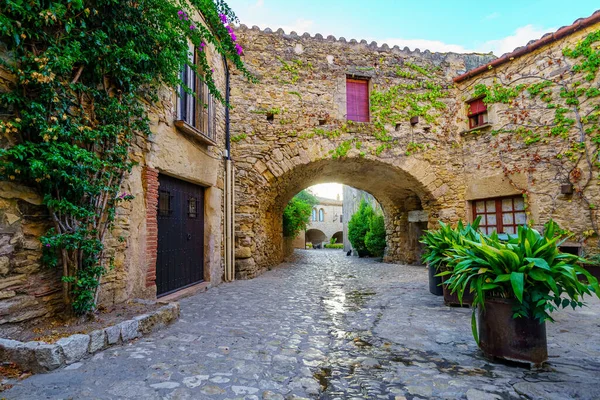 Picturesque alley with stone arches and the sun appearing between the houses at dawn, Peratallada, Girona, Spain