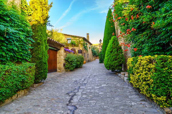 Picturesque alley with stone houses and cobblestone floor, plants and vines at golden sunset, Peratallada, Girona, Catalonia