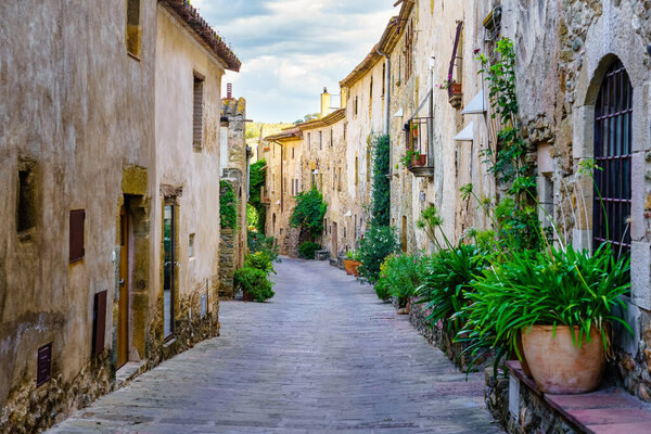 Beautiful alley with old stone houses and pots on the street with plants and flowers, Monells, Girona, Catalonia