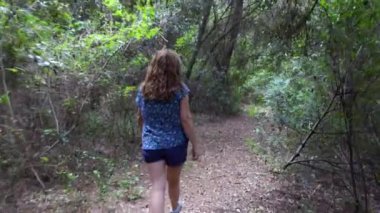 Yolun her iki tarafında da bitkiler ve ağaçlarla orman yolunda yürüyen bir kadın.