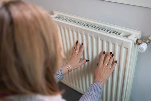 Woman with her hands glued to a radiator to warm them by the cold of winter and the energy savings of the war in Europe