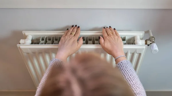 Woman with her hands glued to a radiator to warm them by the cold of winter and the energy savings of the war in Europe