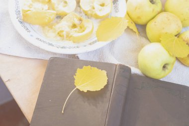 Sarı elmalar ve fırınlanmış elmalar sonbaharda açık bir kitabın yanında, sonbahar yapraklarıyla birlikte bir tabakta uzanıyorlar..