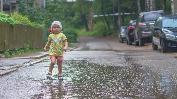 Девочка идет под дождем через лужи летом — стоковое фото