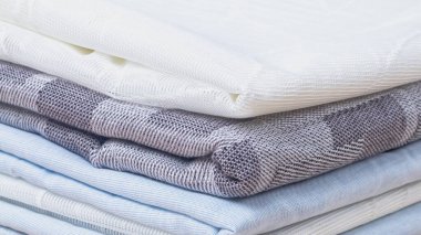 Beyaz, gri, mavi renkte yeni bir kumaş yığını düzgünce katlanmış..