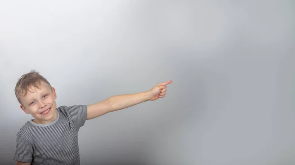 Cheerful Caucasian Boy Smiles Points His Finger Gray Background — Stock Photo, Image