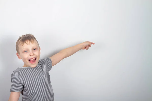 Vrolijke blanke jongen glimlacht en wijst met zijn vinger op een grijze achtergrond — Stockfoto