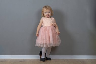 2 yaşında beyaz bir kız çocuğu, siyah annesinin topuklularıyla pembe balo elbisesi içinde yürüyor..