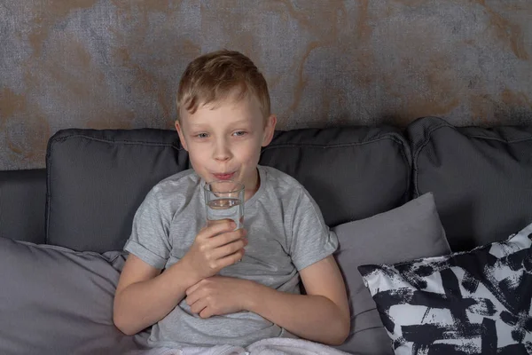 Menino Caucasiano Bebe Água Copo Enquanto Está Sentado Sofá Cinza — Fotografia de Stock