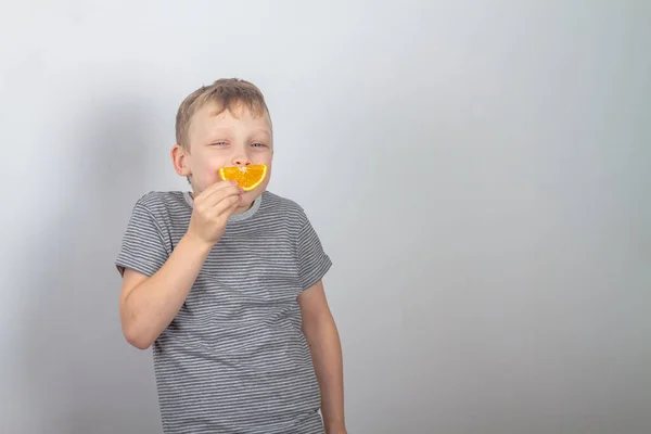 一个快乐的高加索男孩笑了 从灰色背景上的一片橙子里露出笑容 — 图库照片