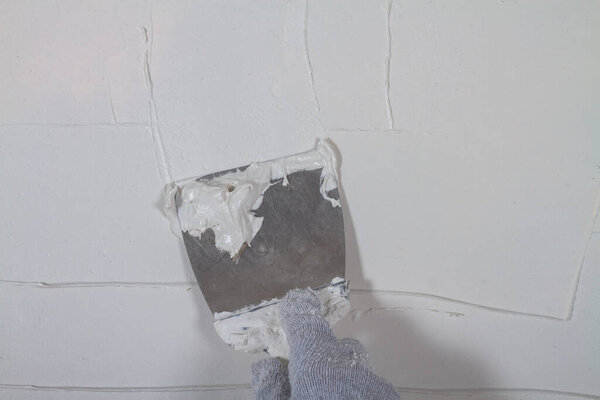 Apply plaster white putty on a concrete wall with a spatula.