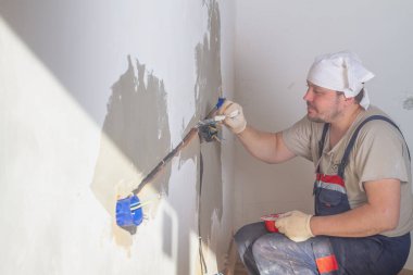 Bir erkek işçi daireye elektrik kabloları ve prizler yerleştiriyor..