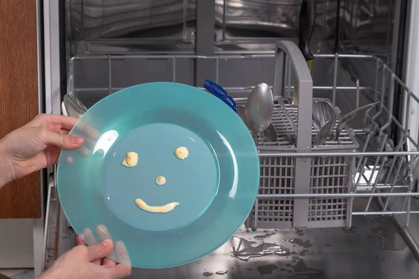 Colocar uma placa azul com uma expressão alegre na máquina de lavar louça para lavar louça — Fotografia de Stock