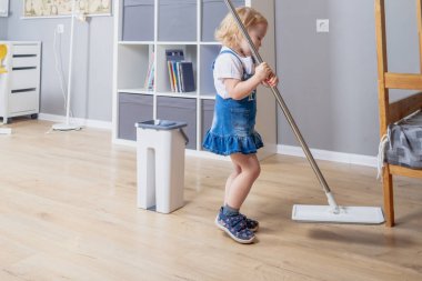 Küçük kız 2 yaşında beyaz tenli. Evin yerlerini paspasla yıkıyor..