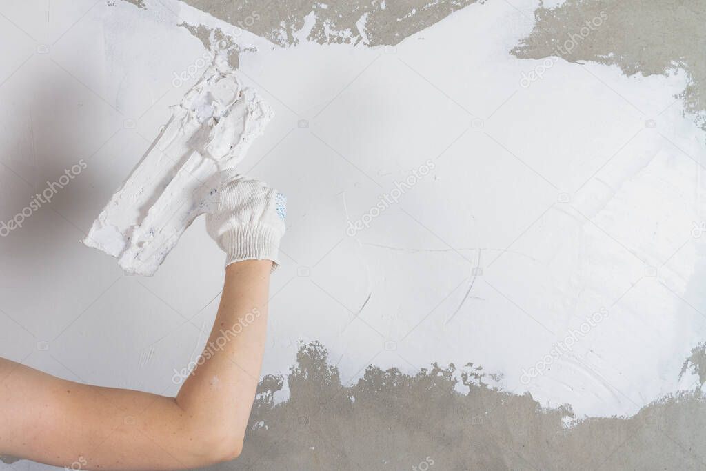 Caucasian female worker putty with a spatula with putty concrete walls in the house.