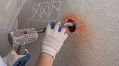 Erkek bir işçi ağır bir balyozla çalışır, tuğla bir duvarı yıkarak elektrik prizi kurar..