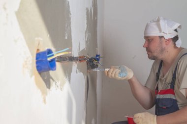 Bir erkek işçi daireye elektrik kabloları ve prizler yerleştiriyor..