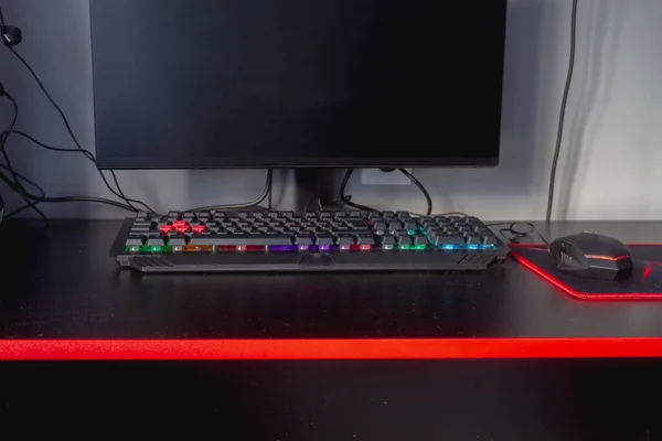 Multi-colored gaming computer keyboard with rainbow backlight on a black table.