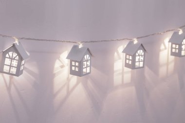 Leylak duvarında beyaz metal evler şeklinde elektrikli çelenkler. Noel arkaplanı.