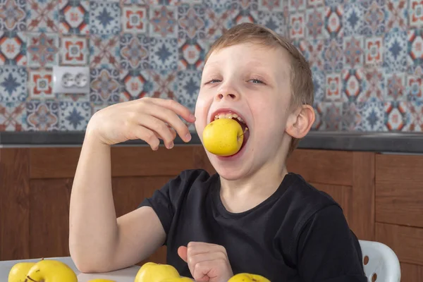 7岁的白人男孩在厨房里吃甜黄色的苹果 — 图库照片