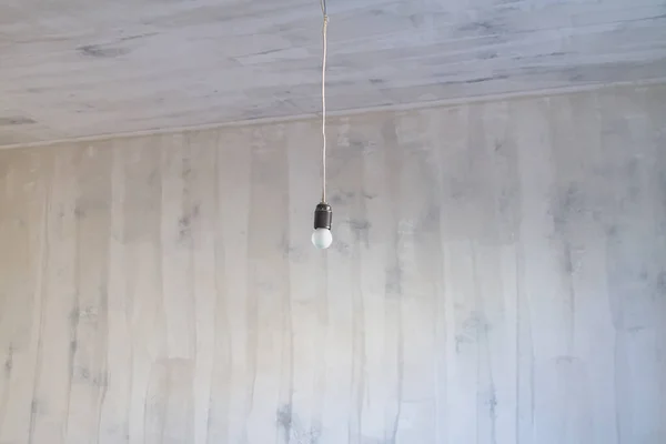 空の部屋の天井にある長い電気ケーブルに電球がかかっています — ストック写真