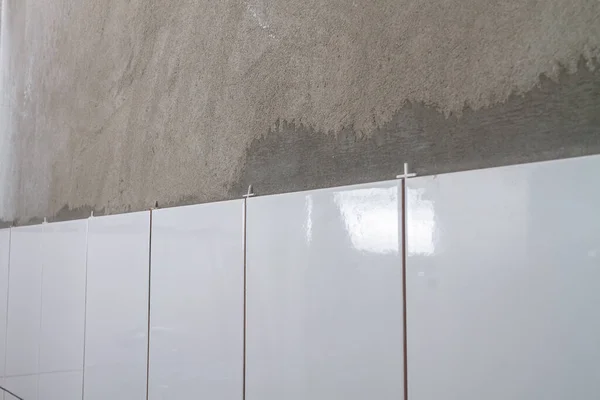 浴室のコンクリート灰色の壁に置かれた白いセラミックタイル 新しいタイル 壁にタイルを敷設するプロセス — ストック写真