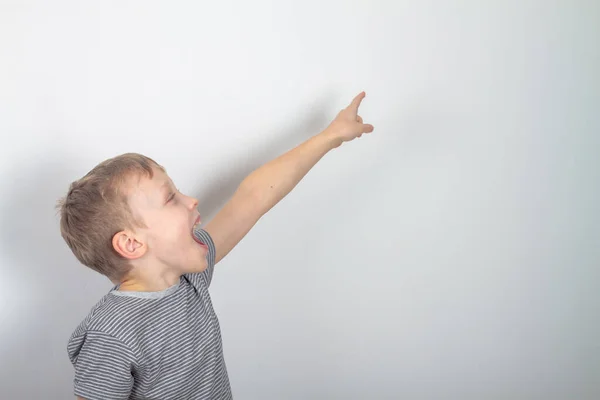 Een blanke jongen in een grijs T-shirt toont zijn vingers naar de zijkant en kijkt naar iets met verrassing en vreugde — Stockfoto