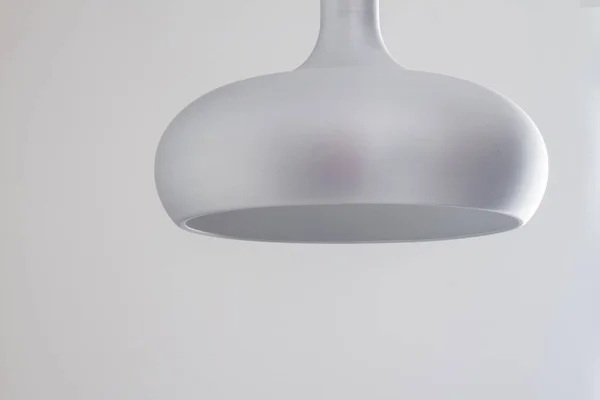 Een zilveren metalen lamp in een eenvoudige halfronde vorm hangt aan het plafond tegen een grijze achtergrond — Stockfoto