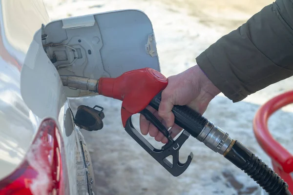 To fill up the car with gasoline at the gas station, a man pours gasoline into the tank of a white car in winter.