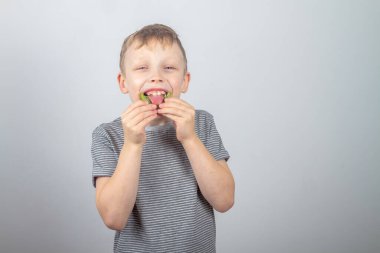 Kafkasyalı bir çocuk yeşil kivi meyvesi yiyor ve gri bir arka planda gülüyor ve gülüyor..