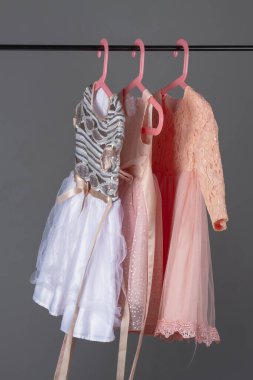 Pembe ve gri pullu lüks elbiseler. Küçük kızlar için. Gri arka planda askılar asılı..