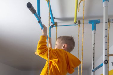 Çocuk kendini evdeki spor kompleksinin yatay çubuğuna çekiyor..