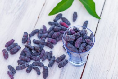 Beyaz ahşap bir masada hanımeli meyveleri, taze bahar mavi böğürtlenler bir bardakta toplanır ve masaya saçılırlar..