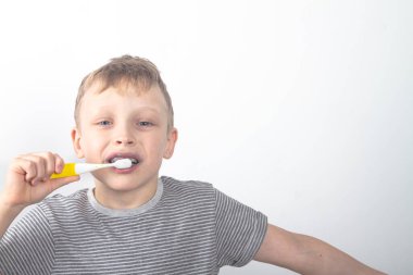 Gri tişörtlü beyaz bir çocuk dişlerini siyah bir kömür diş macunuyla fırçalıyor..