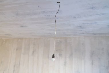 Boş bir odada tavandaki uzun bir elektrik kablosuna asılan bir ampul. .